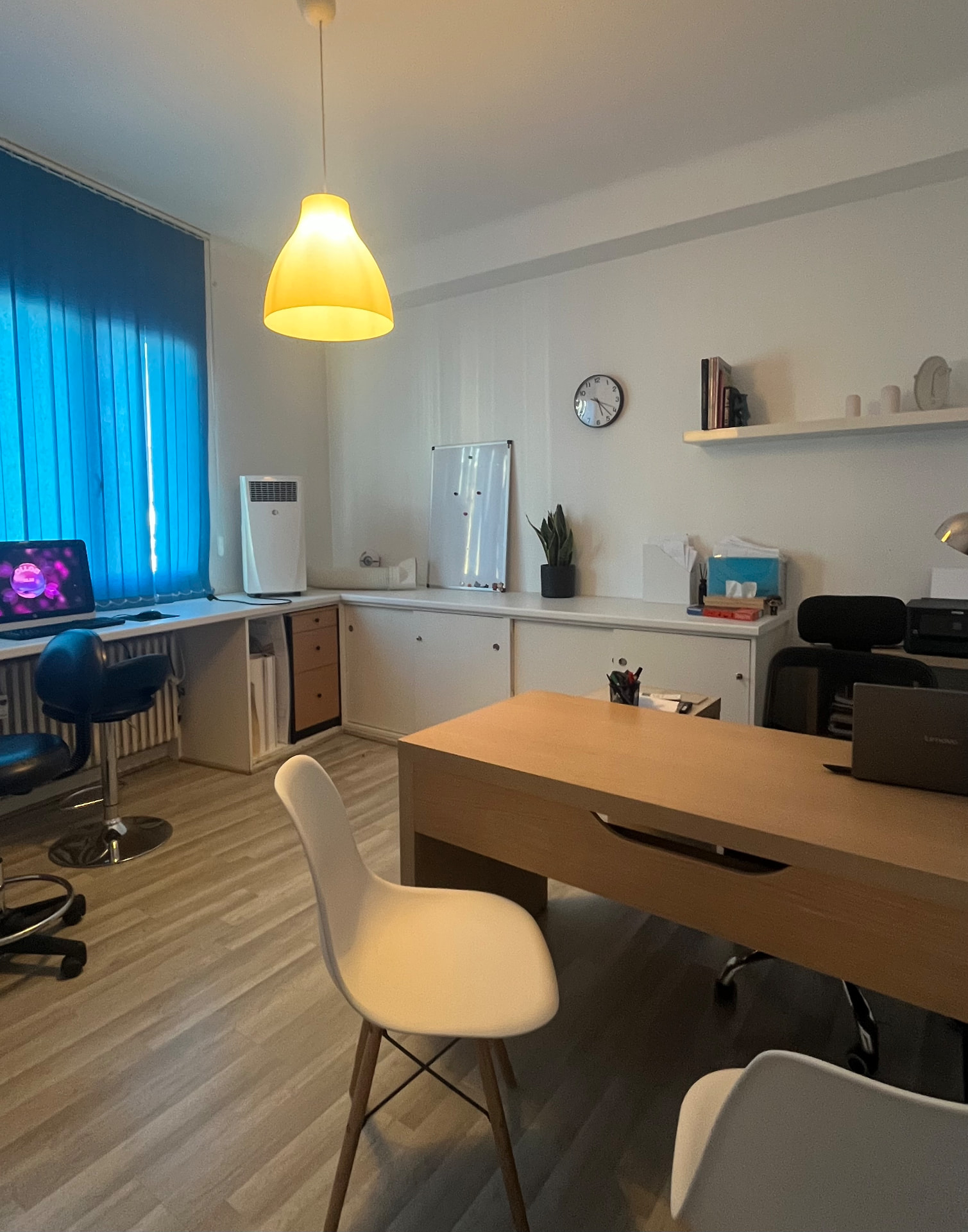 Bureau du cabinet avec table en bois, chaises et rangements blancs sous une suspension lumineuse.